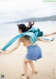 A woman in a bikini top and denim shorts running on the beach.