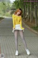 A woman in a yellow sweater and white skirt posing for a picture.