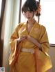 A woman in a yellow kimono standing by a window.