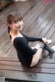 A woman in a black leotard sitting on a wooden floor.