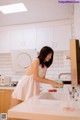 A woman in a white dress is washing her hands in the kitchen.