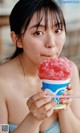 A woman in a blue bikini eating a pink ice cream cone.