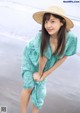 A woman in a blue dress and straw hat on the beach.