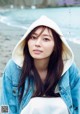 A woman wearing a white hoodie sitting on a beach.