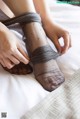 A woman tying up her bare feet on a bed.